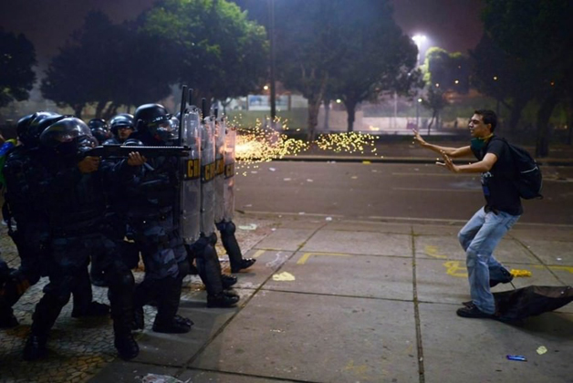 No Brasil, polícia repreende manifestantes de forma agressiva e rapaz, de mãos vazias, enfrenta policiais.