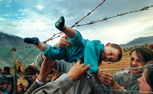 Garoto passa por entre arame farpado para abraçar seus avós durante a guerra de Kosovo