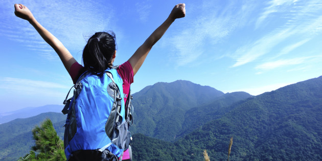 happy hiking woman raised arms at mountain peak
