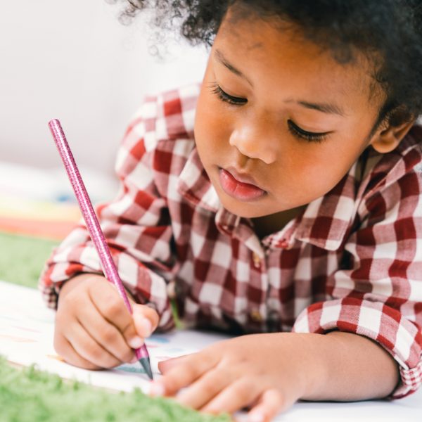 Cute young African American kid girl drawing or painting with colored pencil. Kindergarten children education, back to school, or preschool child study at home concept