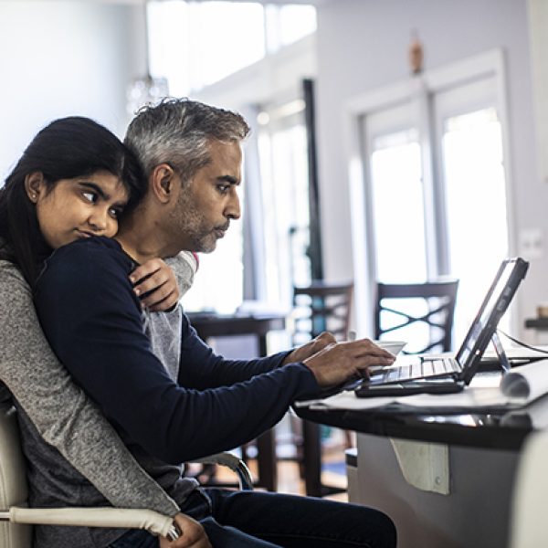 Man working from home in kitchen while teenager daughter distracts him