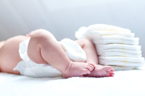 Feet of newborn baby on changing table with diapers. Cute little girl or boy two weeks old. Dry and healthy body and skin concept. Baby nursery