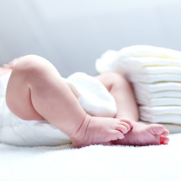 Feet of newborn baby on changing table with diapers. Cute little girl or boy two weeks old. Dry and healthy body and skin concept. Baby nursery