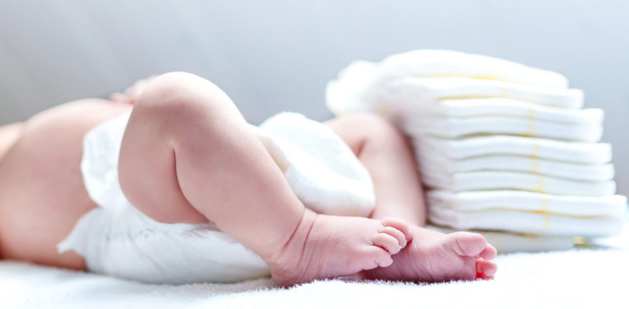 Feet of newborn baby on changing table with diapers. Cute little girl or boy two weeks old. Dry and healthy body and skin concept. Baby nursery